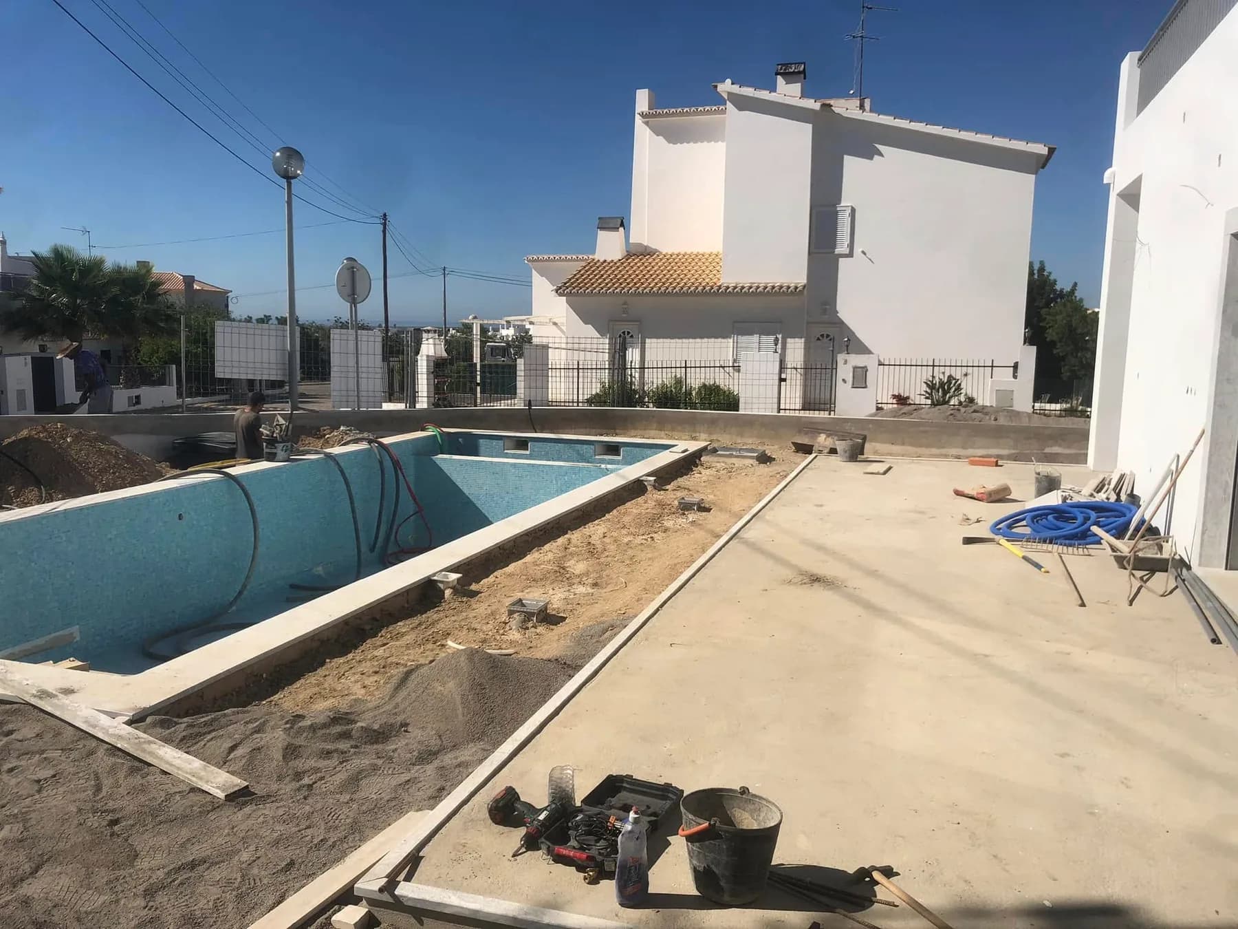 Piscina em construção com mosaico azul junto a moradias brancas